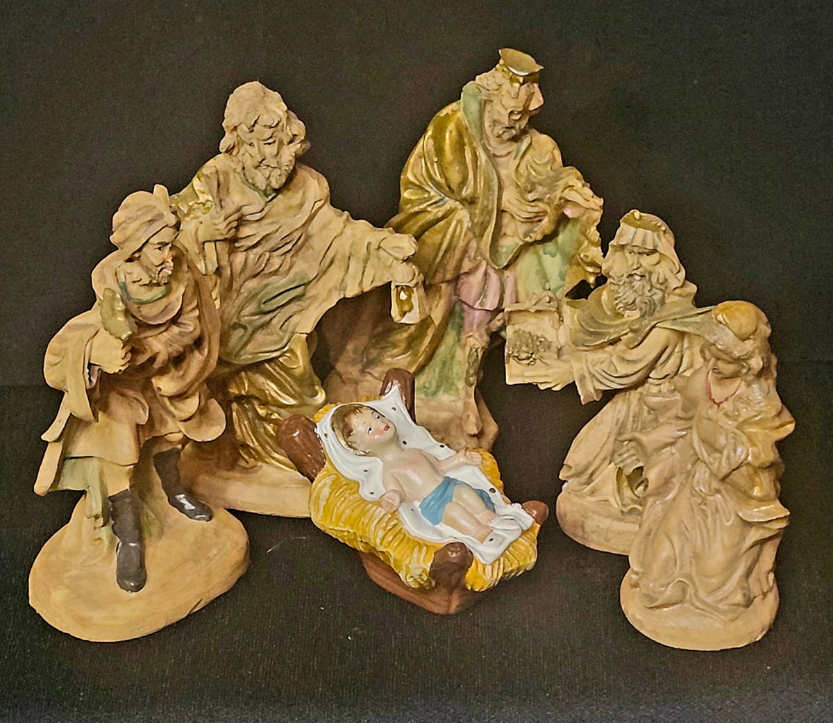 A vintage ceramic nativity scene figurine set featuring multiple characters including wise men, a shepherd, and baby Jesus in a manger, photographed against a dark background.