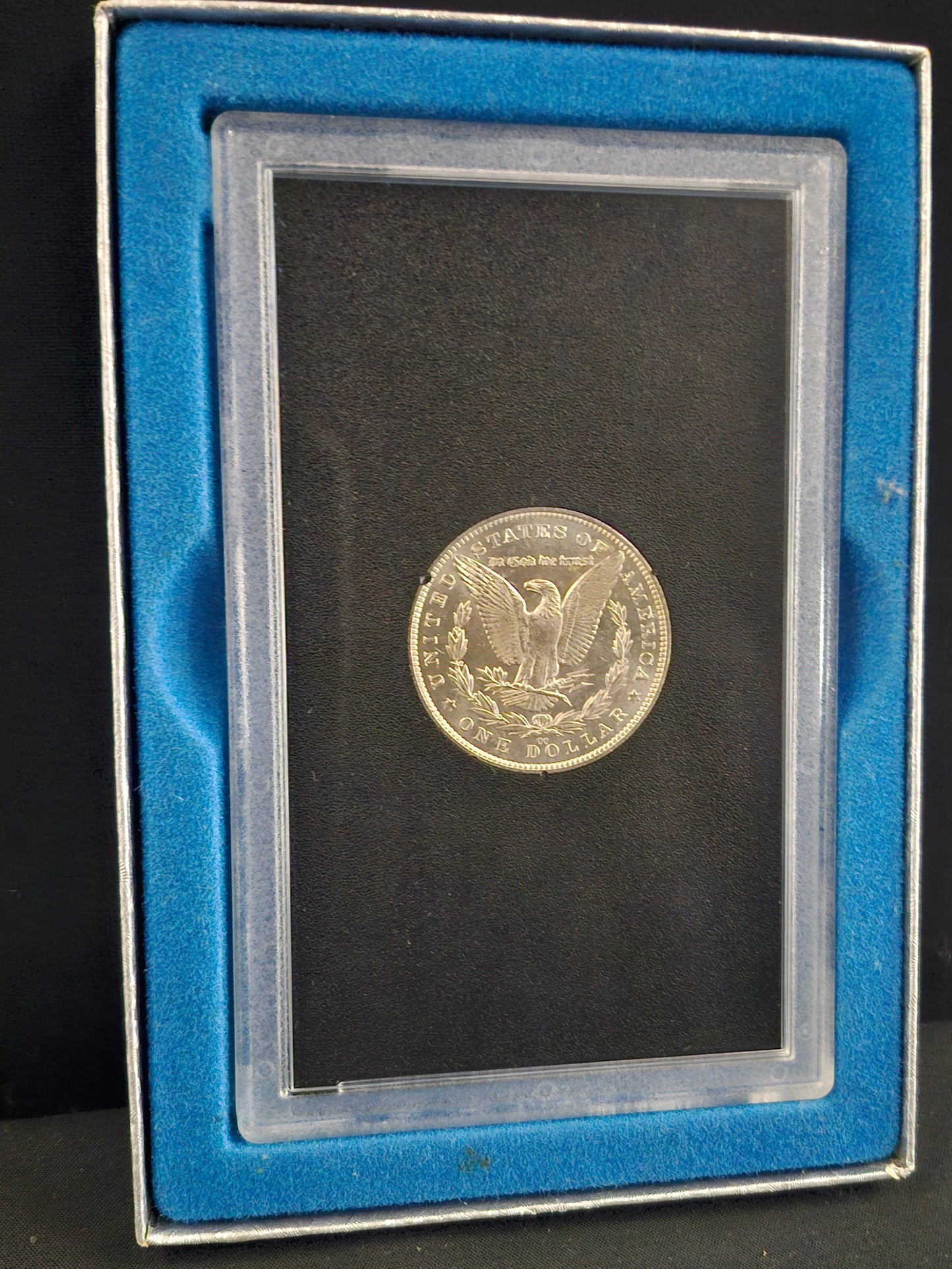 Silver coin in a display case with a certificate on a dark background
