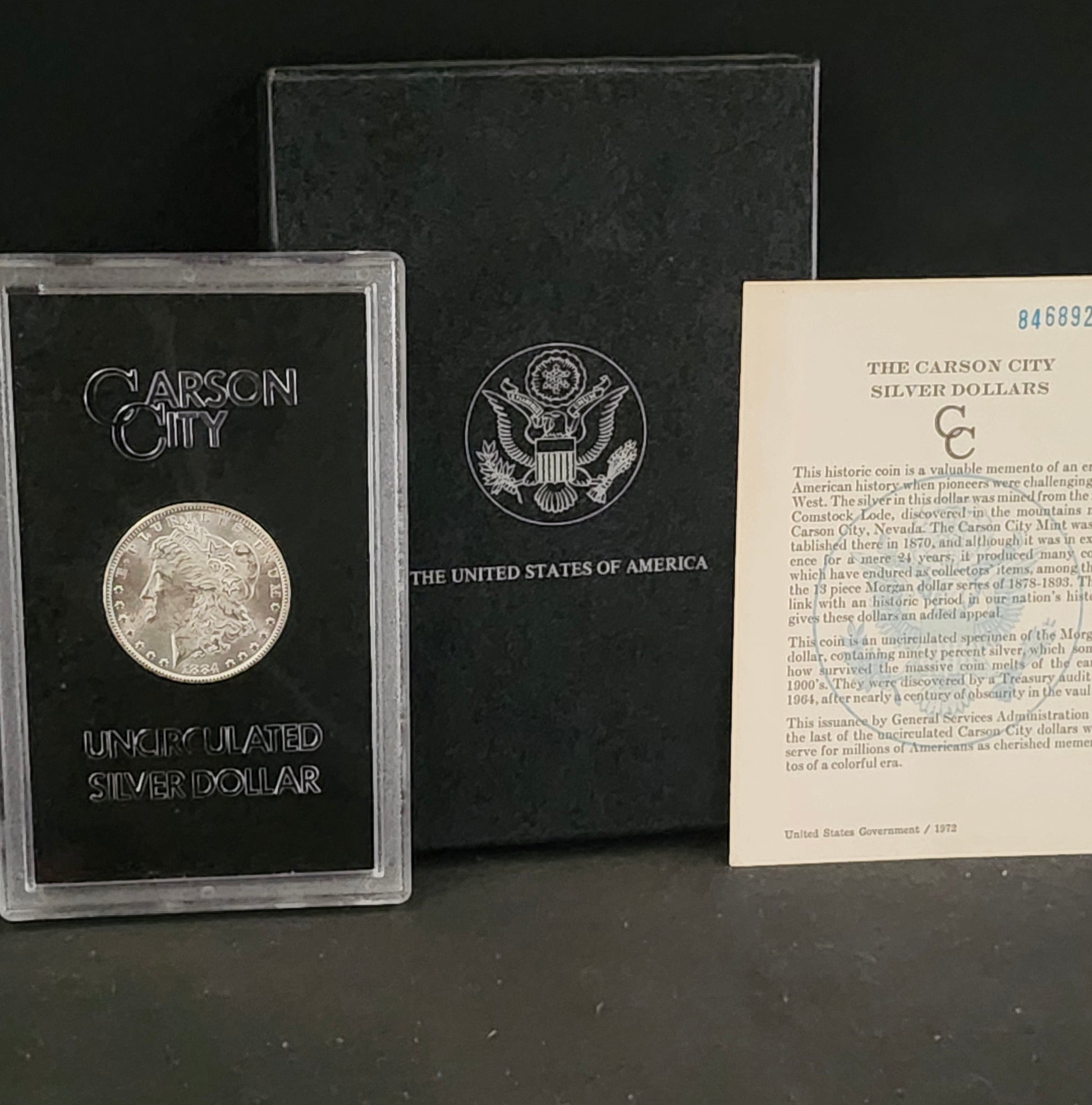 Carson City silver dollar in a display case with an American flag emblem and informational card on a dark background