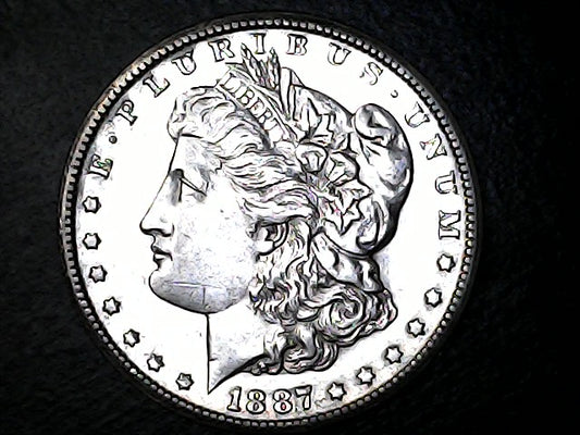 1887 Morgan silver dollar coin with E Pluribus Unum, on a dark background.