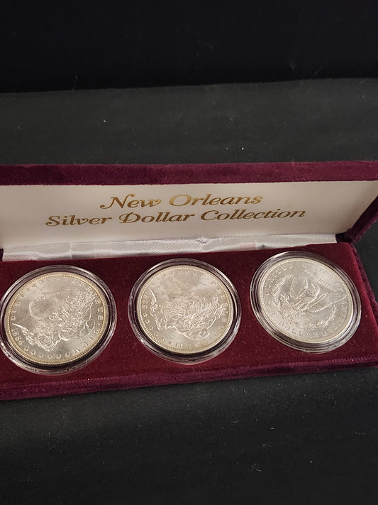 Three silver coins 188-O, 1899-O, 1904-O in a display case with 'New Orleans Silver Dollar Collection' text.