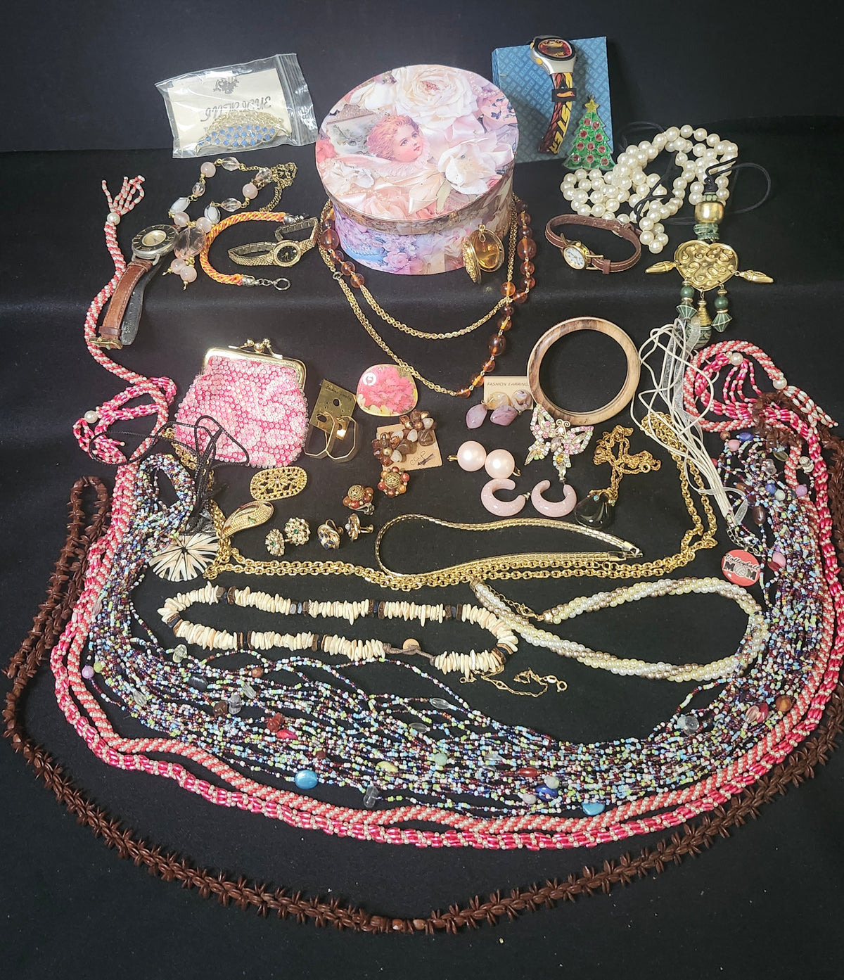 A collection of assorted vintage jewelry and accessories arranged on a black background, including multiple beaded necklaces, pearl strands, bracelets, earrings, a clutch purse, and a round floral hat box.