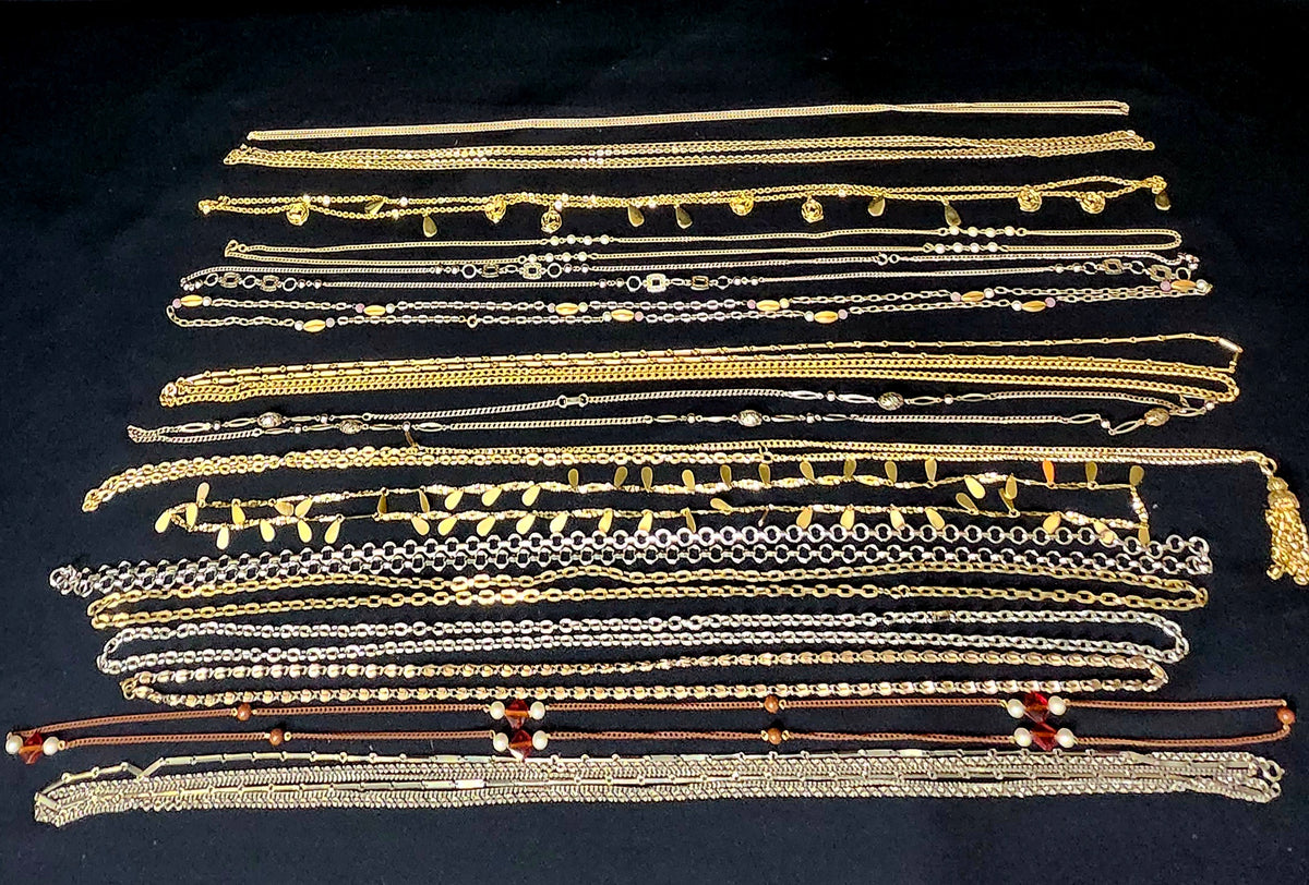 A collection of assorted gold and silver chain necklaces or waist chains arranged flat on a black fabric background.