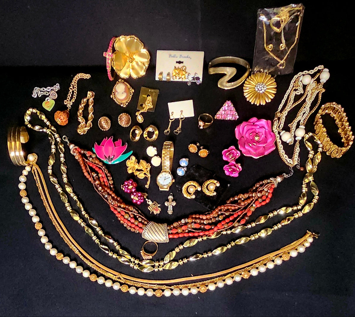 A collection of assorted vintage jewelry items, including multiple necklaces with pearls, beads, and gold-toned chains, bracelets, earrings, rings, and brooches, arranged on a black background.