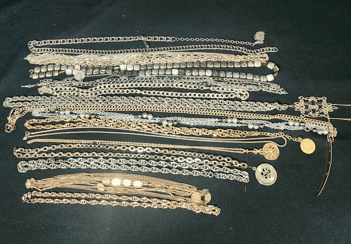 A collection of assorted vintage and antique chain necklaces in silver and gold tones, laid out on a dark black background.