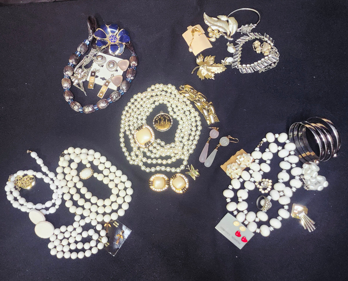 A collection of assorted vintage jewelry items, including pearl strands, beaded necklaces, brooches, earrings, and bracelets, arranged on a black background.