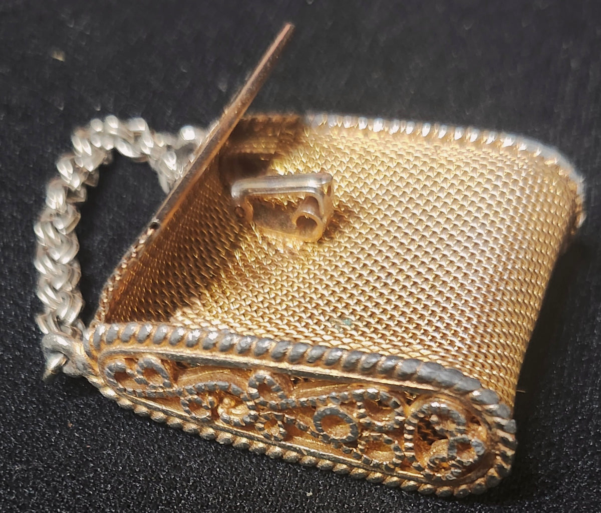 A vintage gold-toned mesh clutch purse with a silver-toned chain handle and ornate filigree trim, photographed on a black textured background.
